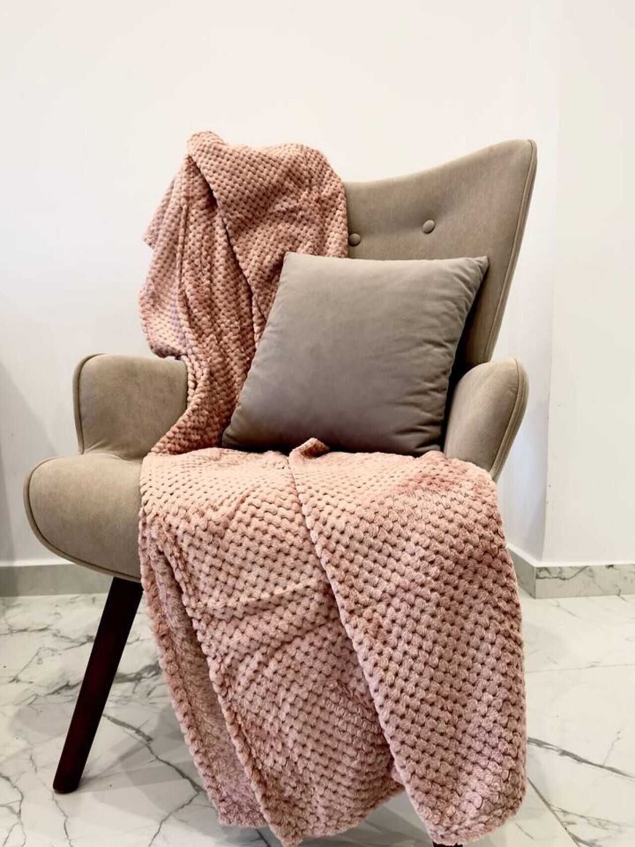 A chair with a knitted blanket and a pillow.