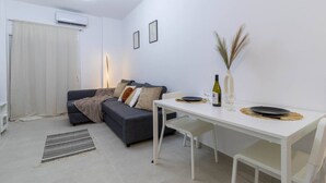 A modern living room with a grey sofa, a white dining table, and a small dining area.