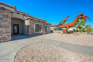 Ein Haus mit Naturstein-Fassade, einer Auffahrt und einer großen Dinosaurierskulptur im Garten.