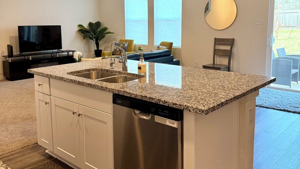 Una cocina moderna con lavavajillas integrado, encimeras de granito y muebles de cocina blancos.