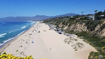 Ein Strand mit blauem Himmel, sandigem Ufer und einigen Gebäuden im Hintergrund.