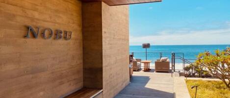 A wooden exterior wall with the name 'NOBU' and a wooden deck leading to a seating area with a view of the sea.