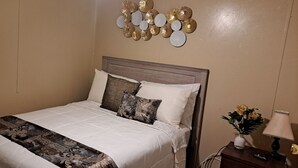 Un lit bien fait, avec une couvre-lit à motifs, une tête de lit et des œuvres d’art décoratives accrochées au mur.
