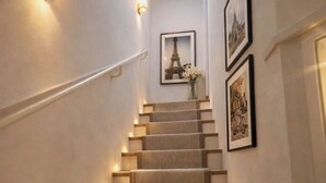 Una escalera con peldaños alfombrados, lámparas fijadas a la pared e imágenes enmarcadas.