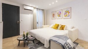 Un dormitorio con una cama, una mesita de noche con una botella y vasos, una silla, una puerta y una ventana.