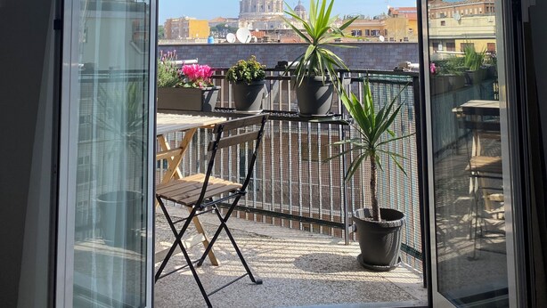 Un balcón con vista a una estructura en forma de cúpula, plantas en macetas y mobiliario de exterior.