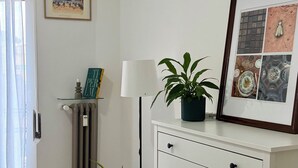 Una habitación con un aparador blanco, un cuadro enmarco, una planta en maceta, un radiador y una ventana con cortinas.