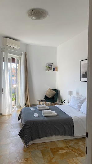 Ein Hotelzimmer mit Bett, Sessel, Nachttisch, Lampe, einem Bild und einer Deckenleuchte.