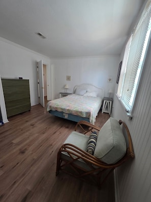 A bedroom with a bed, a chair, a dresser, a nightstand, and a window with blinds. - Rustic, charming beach house straight out of Old Kitty Hawk. Ocean views (Kitty Hawk)