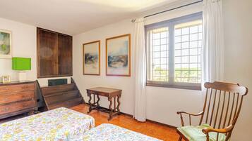 A bedroom with two beds, a wooden chair, a small table, a dresser, and a window with curtains.
