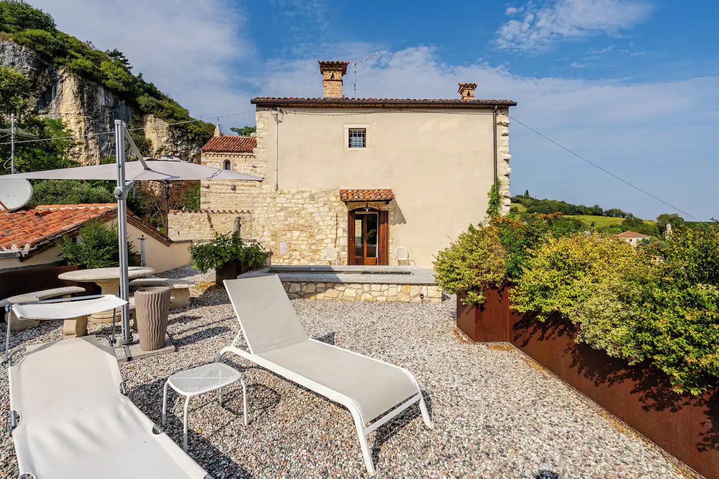 A stone building with a tiled roof, a door, and a small window. There are outdoor seating areas with chairs and tables.