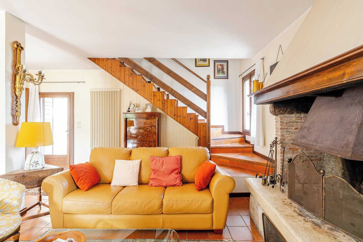 A living room with a yellow sofa, a fireplace, a staircase, and a wooden ceiling.