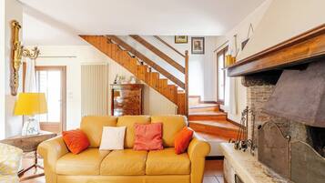 A living room with a yellow sofa, a fireplace, a staircase, and a wooden ceiling.