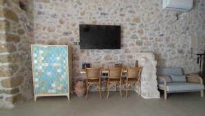 Een kamer met een stenen muur, een flatscreen televisie boven een houten tafel met stoelen, een blauw patroonkast en een lichtblauwe bank.