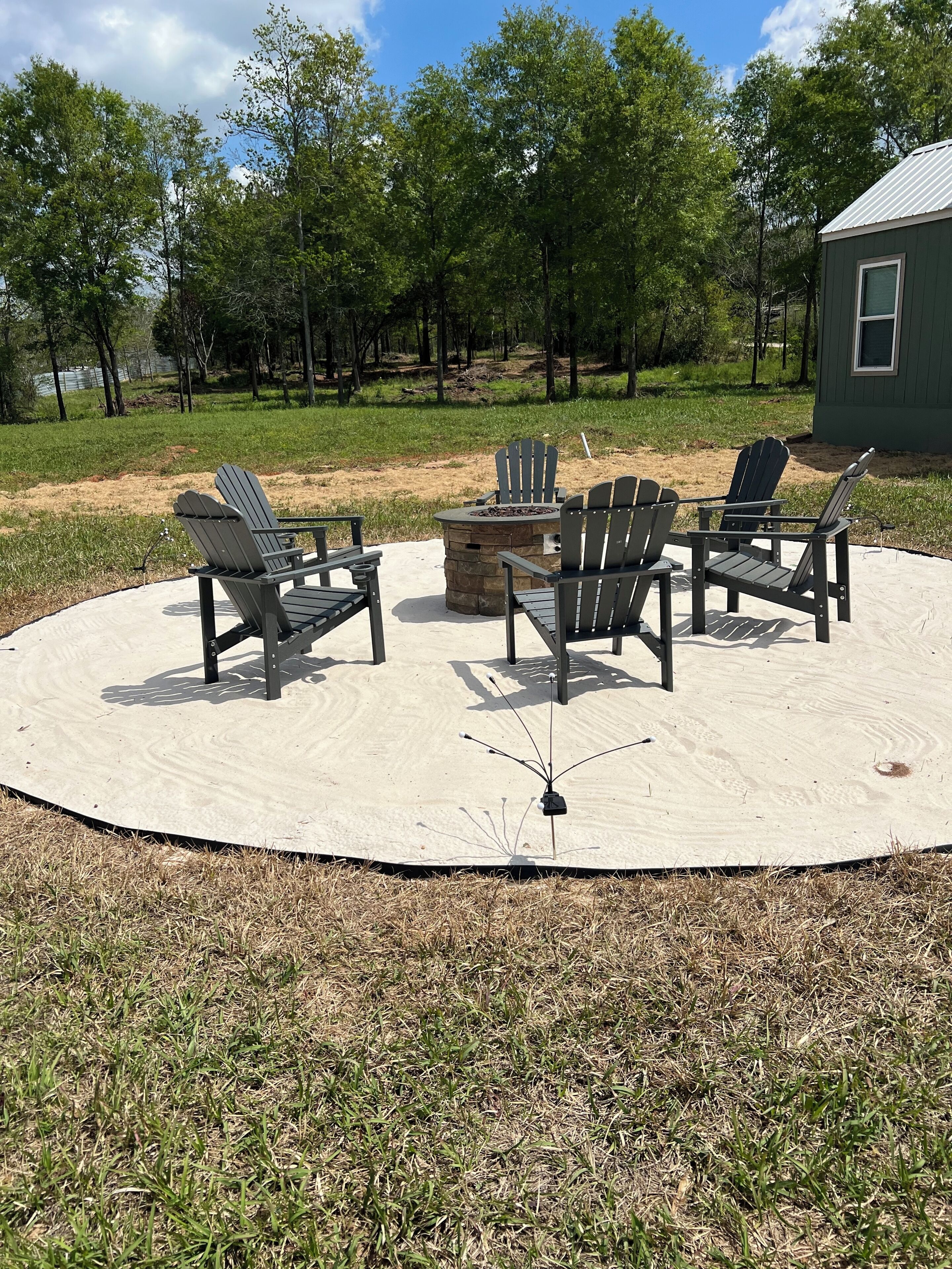 A circular outdoor seating area with Adirondack chairs and a fire pit, surrounded by a sandy deck.