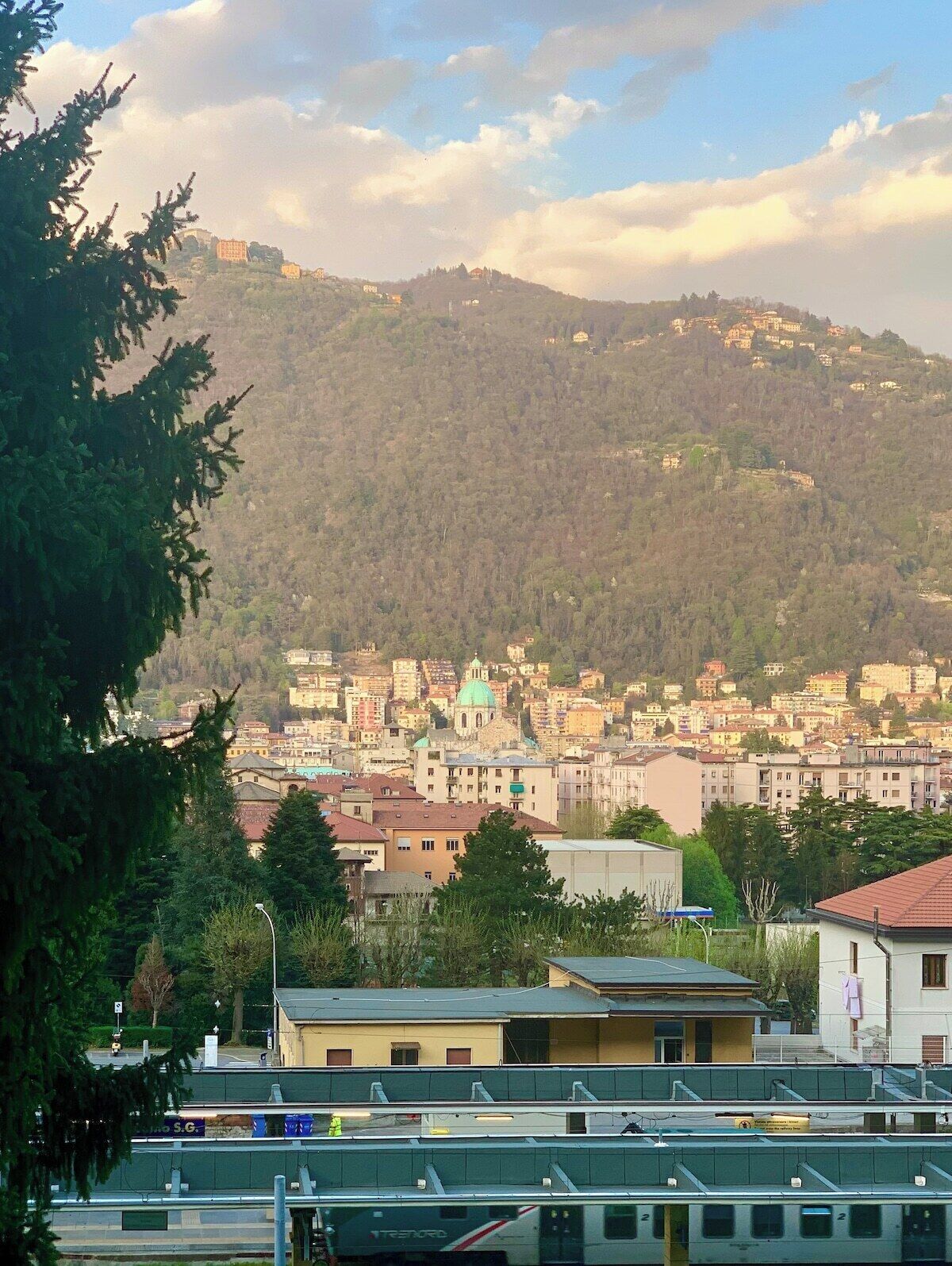 Une vue urbaine avec des bâtiments, une colline en arrière-plan et un train au premier plan.