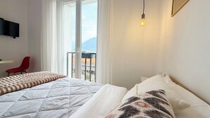 Une chambre d’hôtel avec deux lits, un fauteuil rouge, un téléviseur fixé au mur et un balcon avec vue.