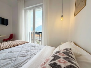Ett hotellrum med två sängar, en röd fåtölj, en tv som är monterad på väggen och en balkong med utsikt.