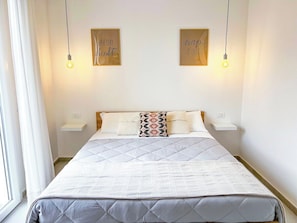 A neatly made bed with a quilted headboard, two bedside tables, and two wall-mounted light fixtures.