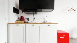 Une cuisine avec des meubles blancs, une hotte noire, un appareil électroménager rouge et un plan de travail en bois.