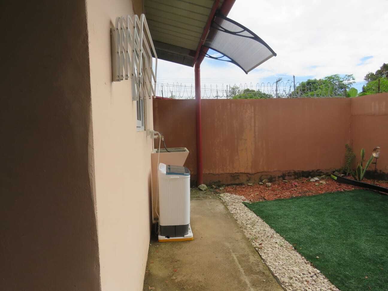 A covered outdoor area with a white appliance, a metal railing, and a green artificial turf lawn.