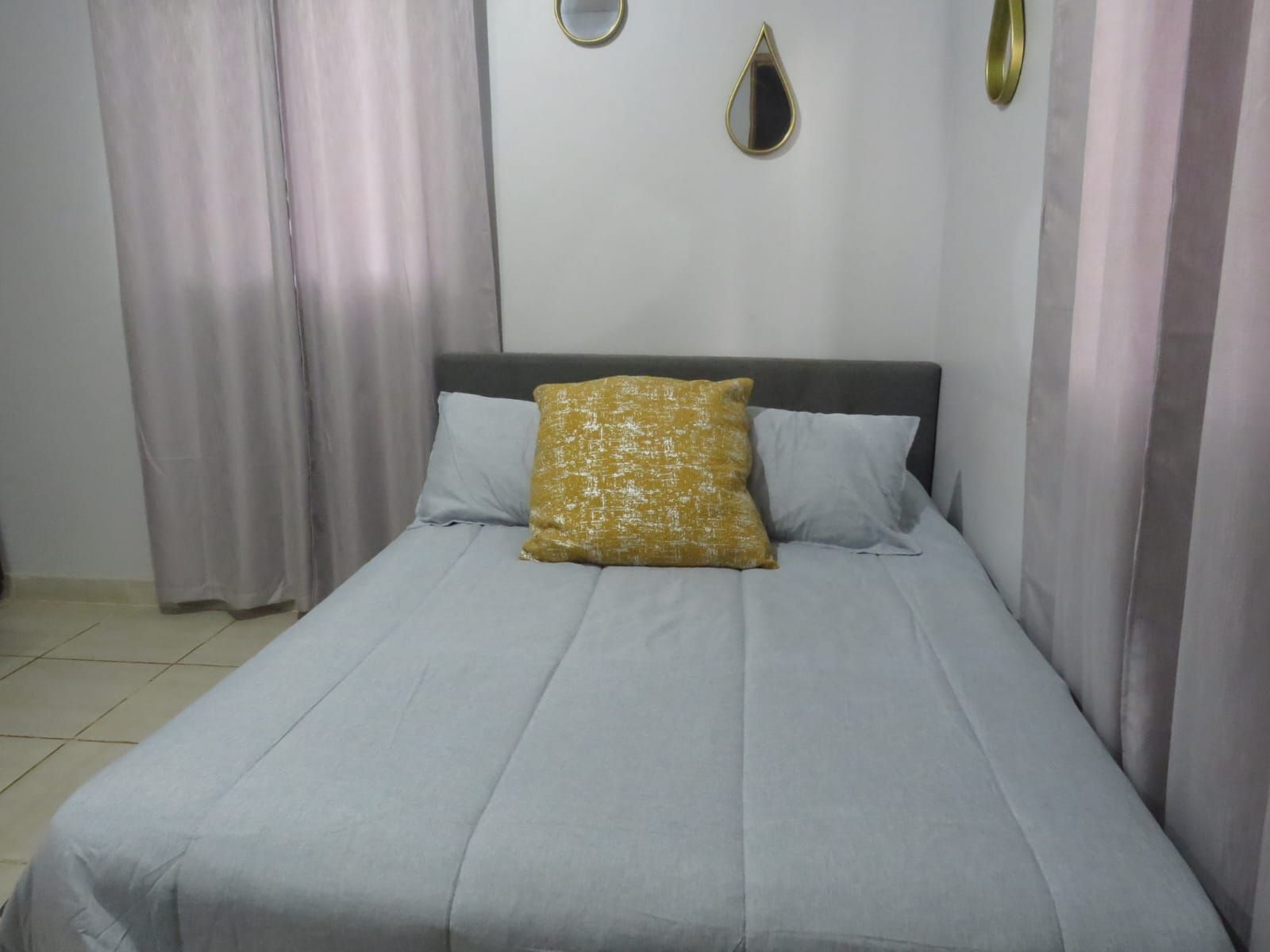 Un lit avec une couvre-lit grise et deux oreillers, dont l’un présente un motif texturé.