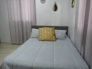 A bed with a grey bedspread and two pillows, one with a textured pattern.