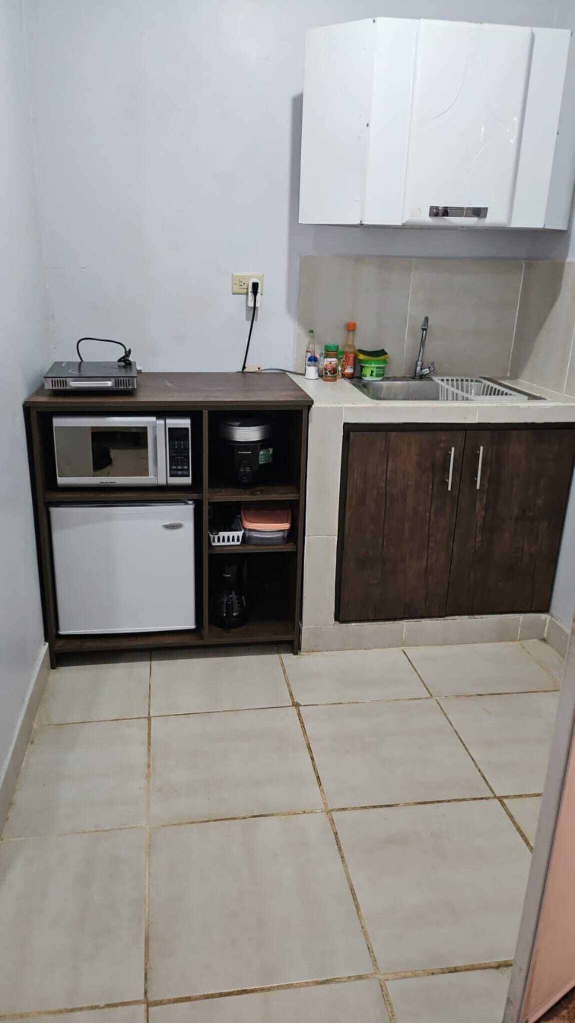 Een kleine keuken met een magnetron, koelkast en een spoelbak.