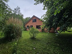 Ein Ziegelhaus mit geneigtem Dach, umgeben von einer gepflegten Rasenfläche und üppiger Bepflanzung.
