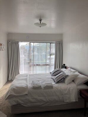 Ein Schlafzimmer mit Bett, Deckenventilator, Fenster mit Vorhängen und Blick nach draußen.
