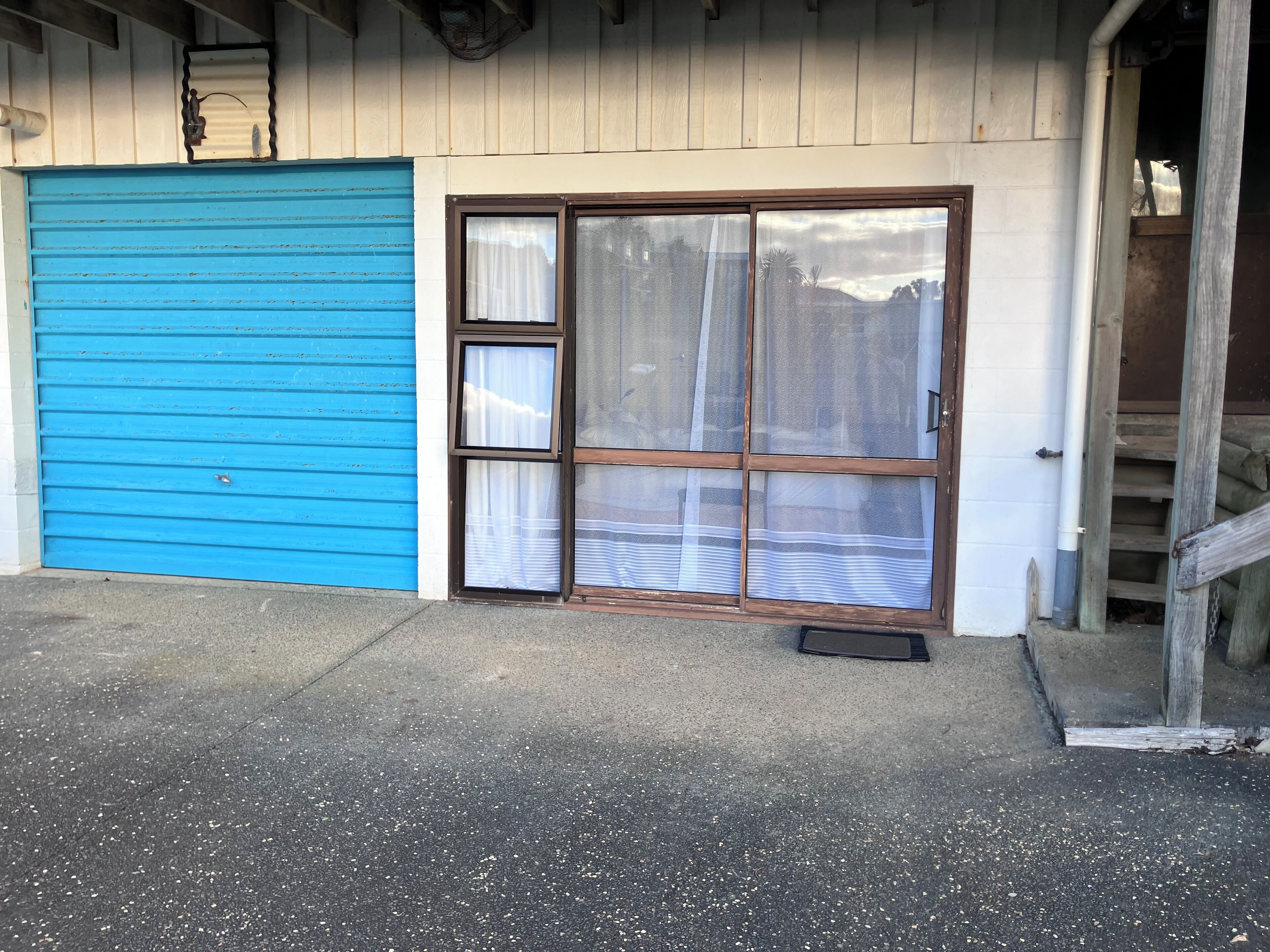 Een gebouw met een blauwe garageklep, dubbele deuren met een raam en een betonnen grond.