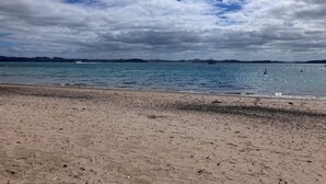 A beach with a sandy shore, calm water, and distant hills.