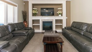 A living room with two leather sofas, a wooden coffee table, a fireplace, and a flat-screen TV above the mantel. - Executive lodging (Edmonton)