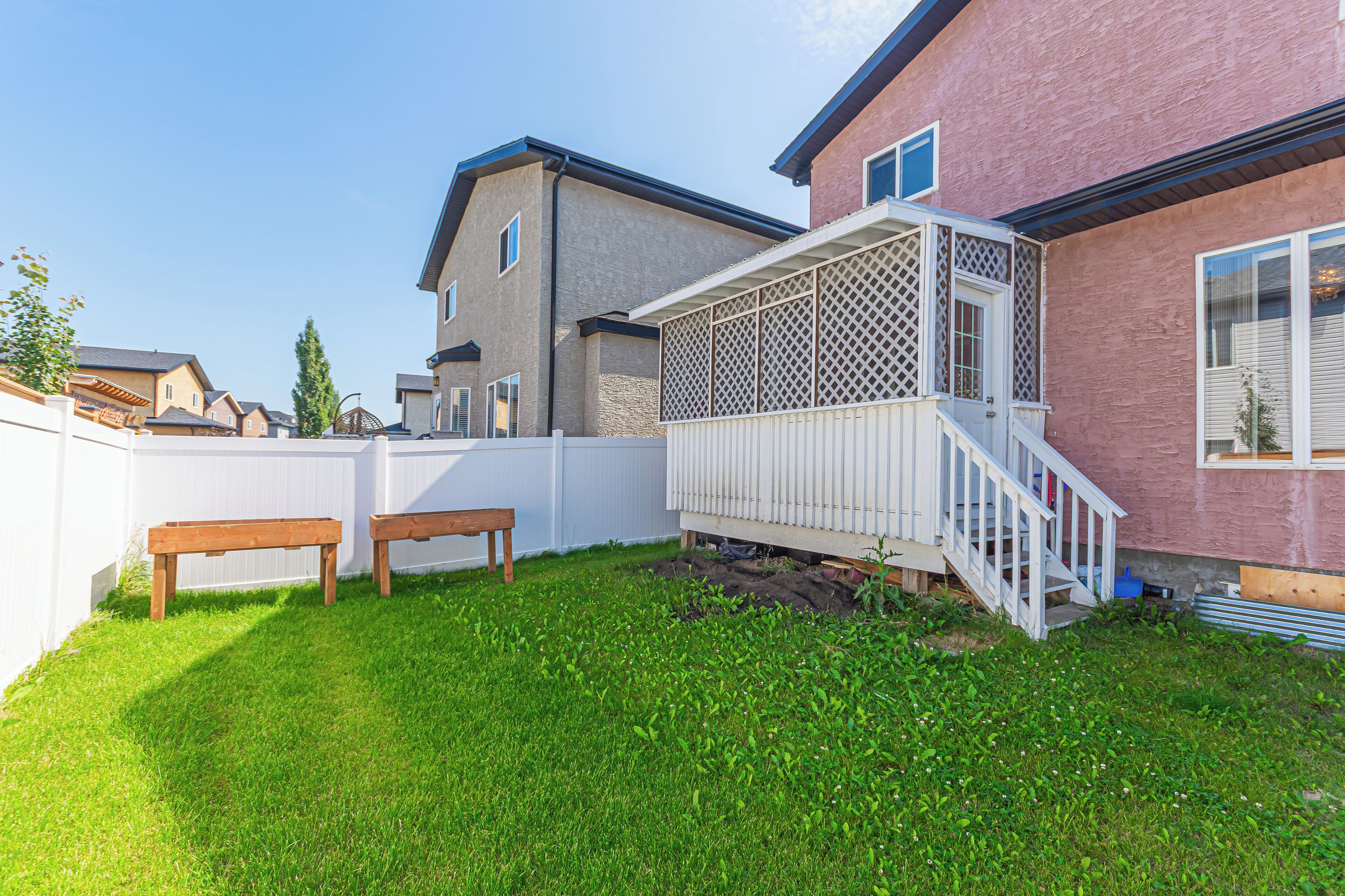 A backyard with a wooden deck, a white fence, and a red building.