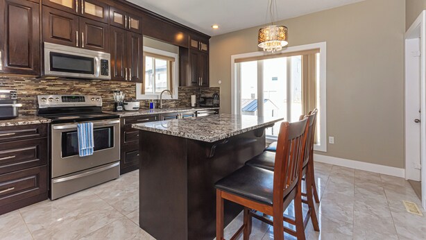 A modern kitchen with dark wood cabinets, stainless steel appliances, and a large island with bar seating. - Executive lodging (Edmonton)