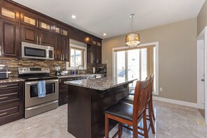 A modern kitchen with dark wood cabinets, stainless steel appliances, and a large island with bar seating.