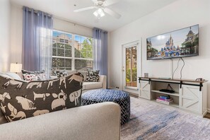 Ein Wohnzimmer mit einer Couch, einem Hocker, einem Fernseher und Blick auf ein Schloss.