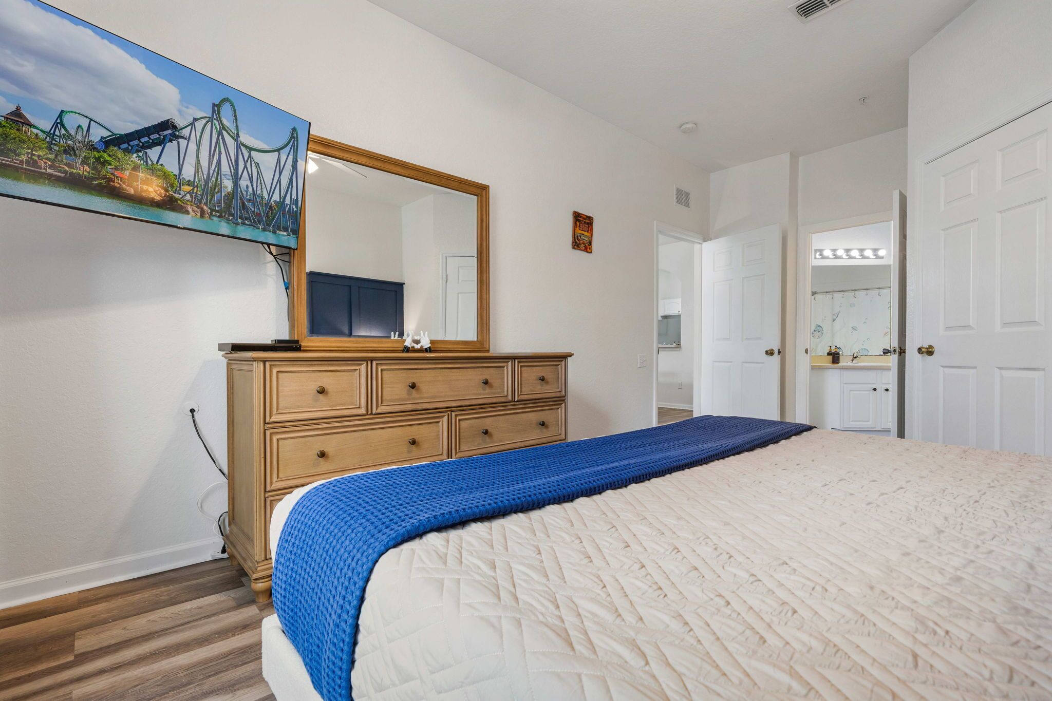 A bedroom with a bed, a dresser, a mirror, and a painting of a roller coaster.