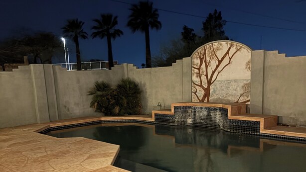 A swimming pool with two lounge chairs, a tiled deck, and a decorative wall with a tree mural.