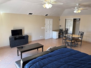 A bedroom with a bed, a desk, a chair, a television, and a ceiling fan.