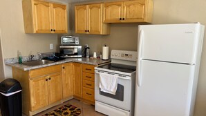 A compact kitchen with wooden cabinets, a microwave, a stove, and a refrigerator.