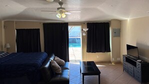 A room with a bed, a desk, a ceiling fan, and a view of the outdoors.