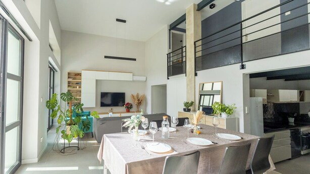 Een moderne eetruimte met een lange tafel voor zes personen, omringd door stoelen. Achtergrond toont een keuken met een zwart aanrecht en roestvrijstalen apparatuur.