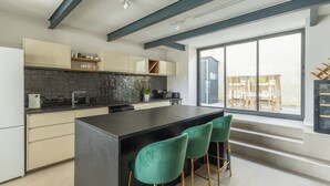 Een moderne keuken met een groot eiland, barstoelen en uitzicht op de omgeving door grote ramen.