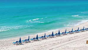 Una playa con hileras de sillas y sombrillas azules, una orilla arenosa y el océano.
