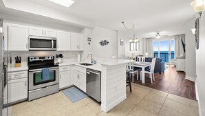 Una cocina moderna con armarios blancos, microondas integrado y lavavajillas. Cuenta con un comedor con mesa y sillas, y vista al océano a través de amplias ventanas.