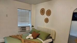 Ein Schlafzimmer mit einem Bett, einem Fenster mit Jalousien, einer Klimaanlage und drei Wanddekorationen.