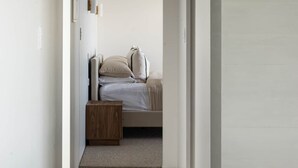 A narrow hallway leading to a bedroom with a bed, a nightstand, and a small wooden table. - The Hide Kapiti Accommodation (Maungakotukutuku)
