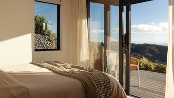 A bedroom with a large bed, a window with a view of a rocky landscape, and a sliding glass door leading to an outdoor deck.