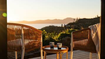 Wicker chairs with a small table and two patterned cups on a wooden deck overlooking a scenic landscape.